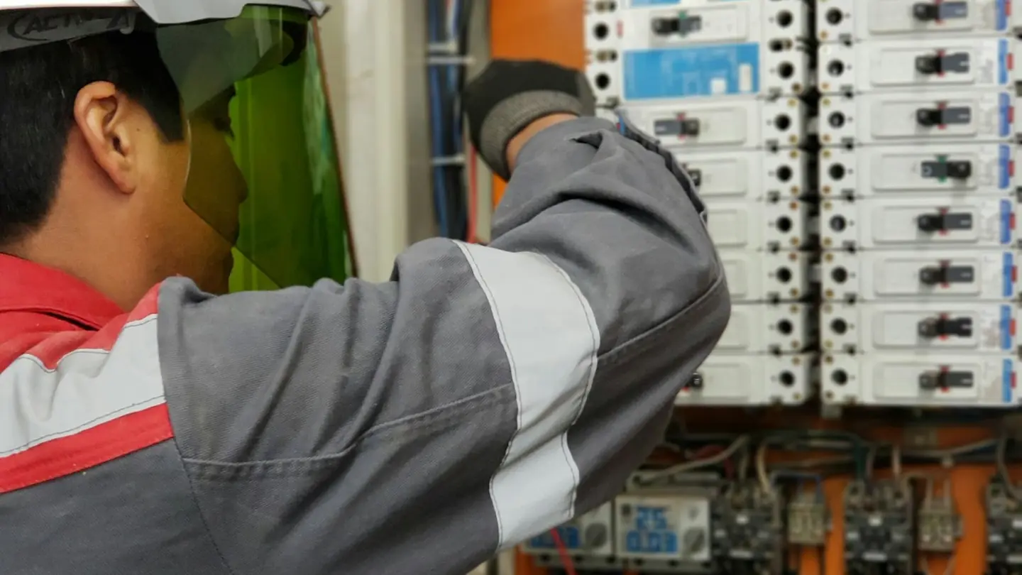Electrician in hard hat and face shield testing a bank of electrical panels